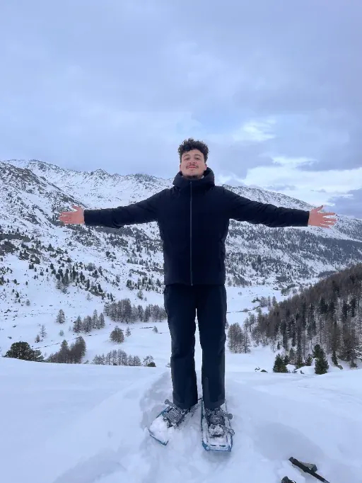 Yacine en randonnée en raquettes, bras ouverts face à la montagne enneigée